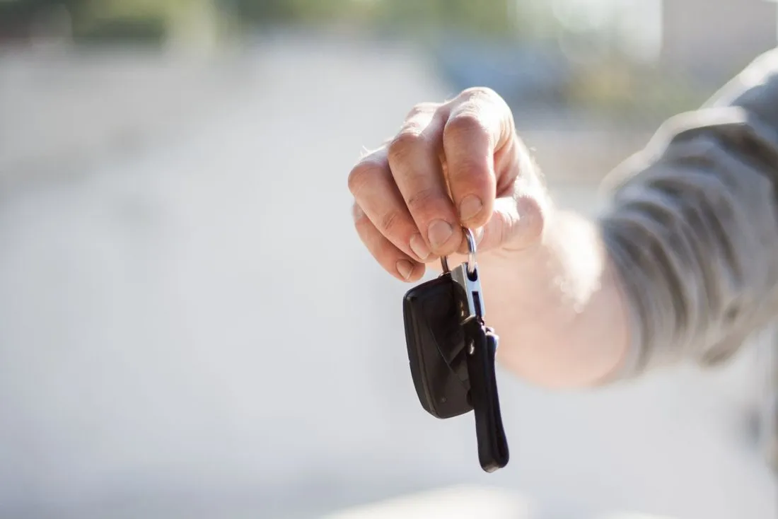 A hand holding out a set of car keys, ready to hand them over
