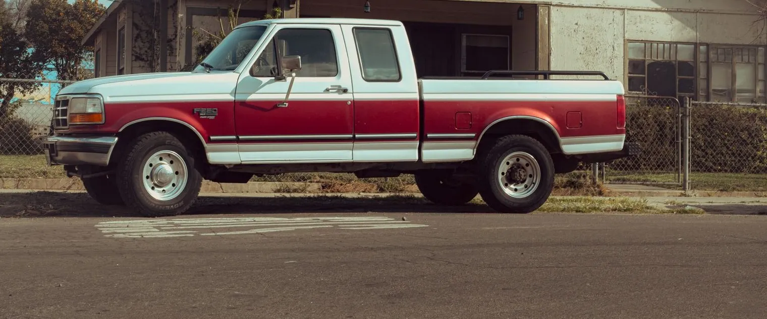 An older red and white pickup truck parked at the curb in front of a house on a sunny day